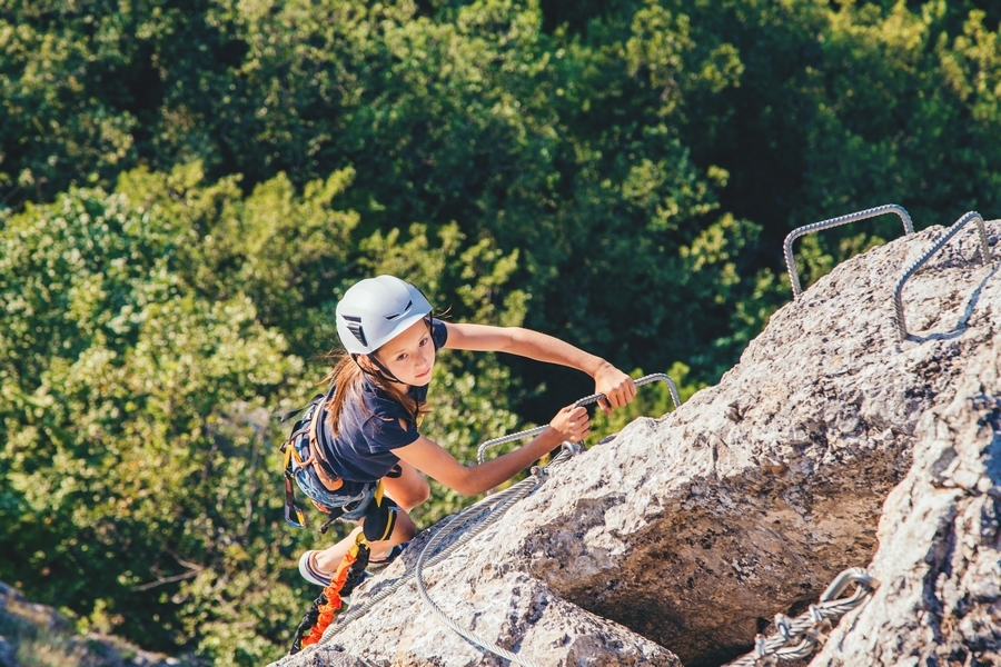 une jeune fille casquée monte les barreaux soudés dans le rocher de la via-ferrata